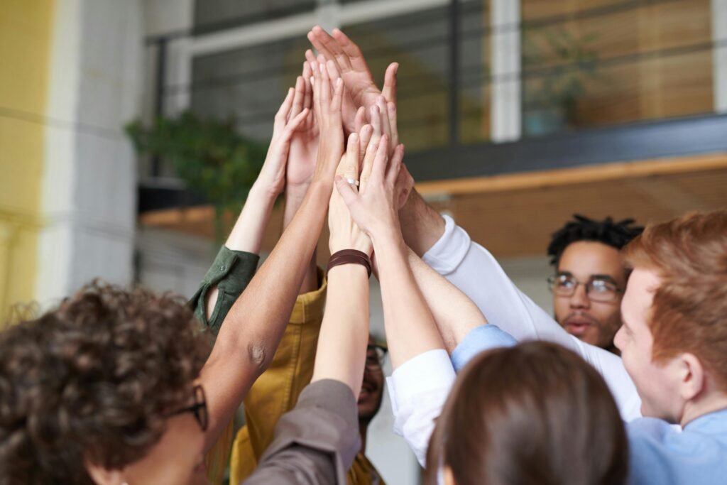 pexels-photo-3184428-3184428 A group of diverse professionals celebrating teamwork with a high-five indoors.