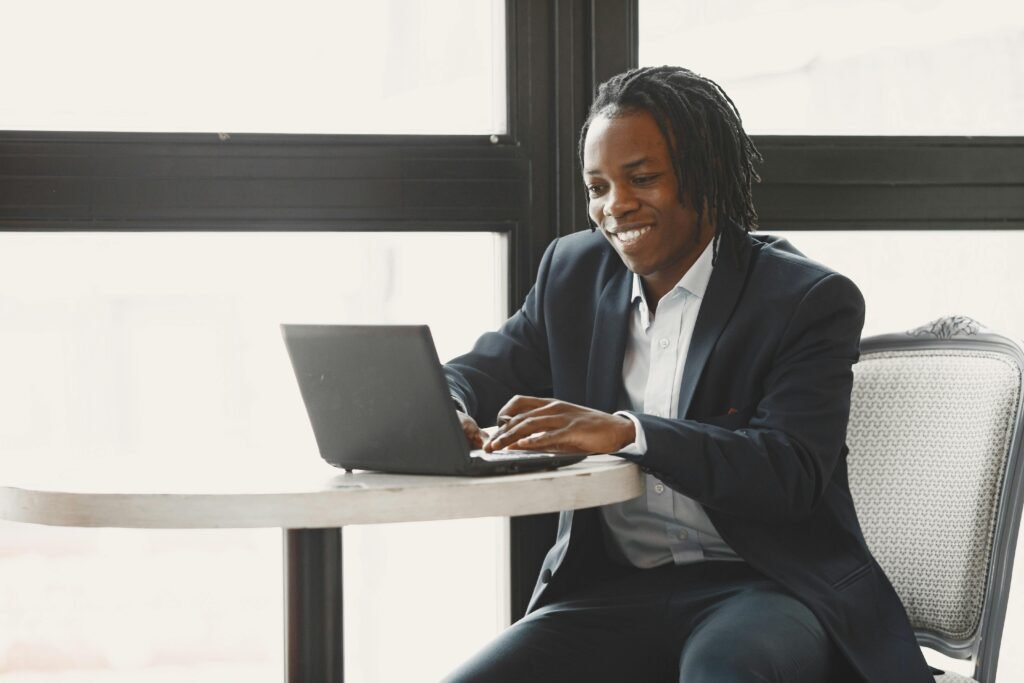 Smiling man in a suit working on a laptop at a table in a modern office setting.