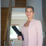 Smiling woman in pink blazer holding a document indoors, exuding confidence and professionalism.